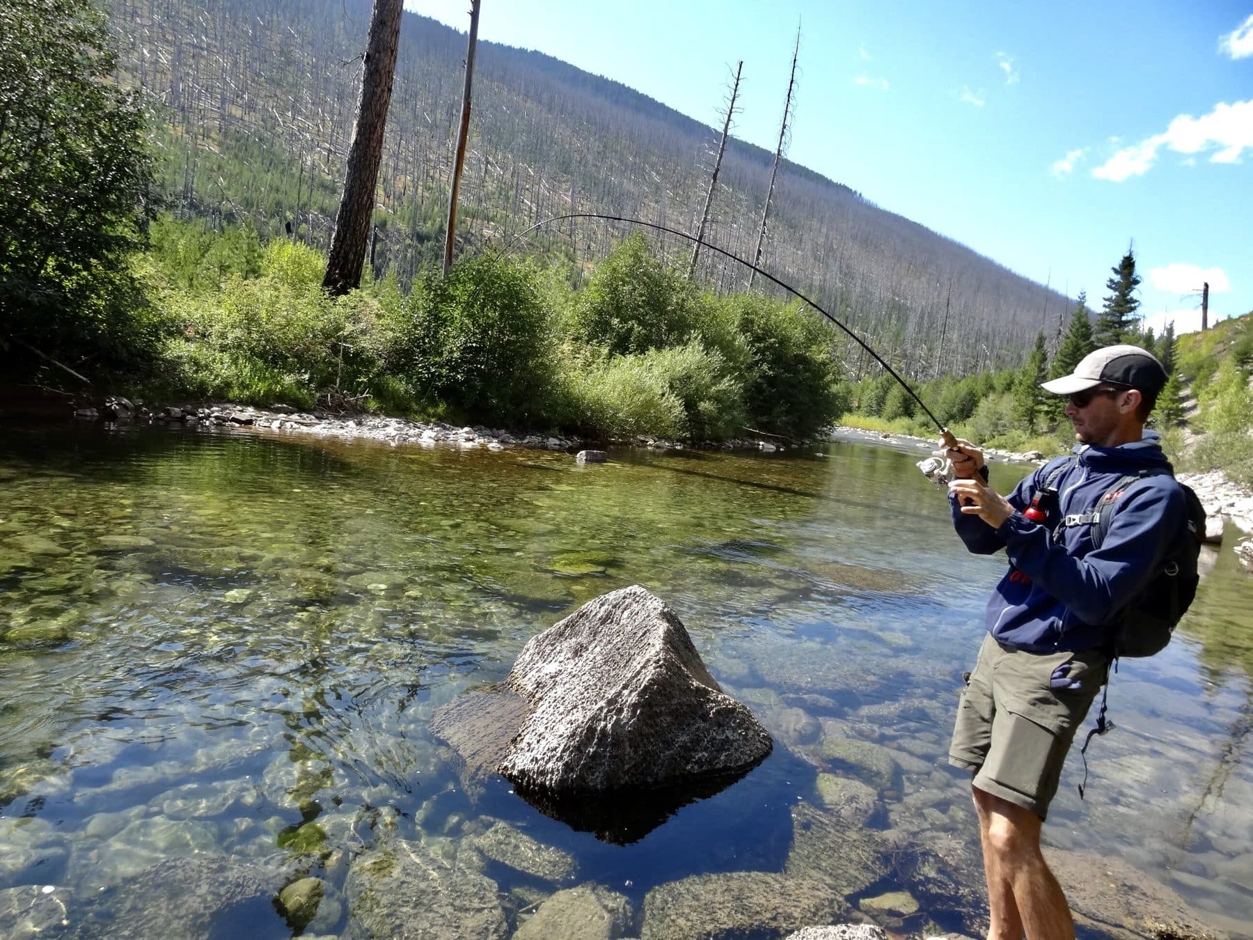 An angler fighting a fish on a rocky river bend